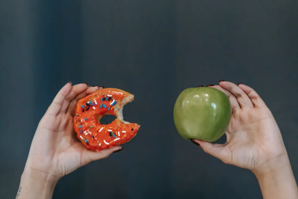 A donut and green apple held between fingers.